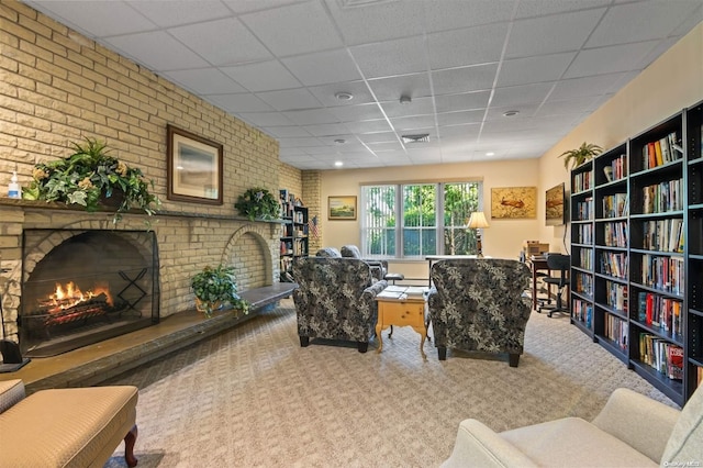 carpeted living room with a fireplace, a drop ceiling, and brick wall