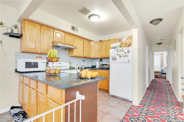 kitchen with dark stone countertops, white appliances, decorative backsplash, light brown cabinetry, and light tile patterned floors