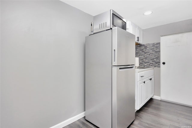 kitchen with decorative backsplash, stainless steel fridge, light wood-type flooring, and white cabinetry