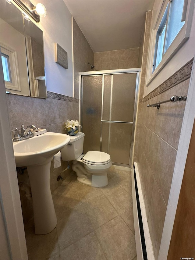 bathroom with tile patterned floors, toilet, a shower with shower door, and tile walls