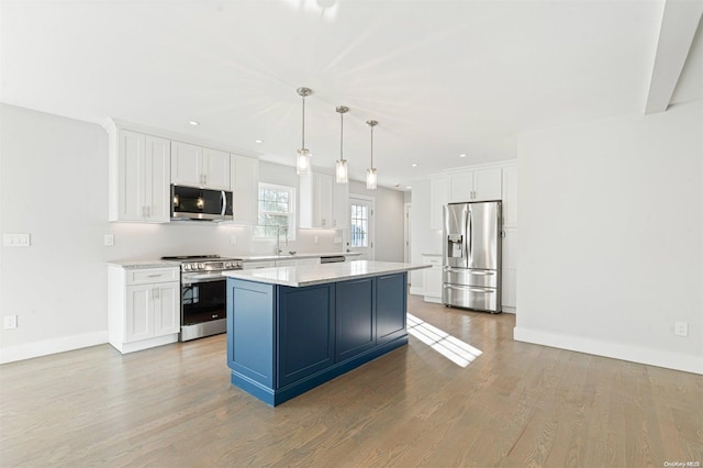 kitchen featuring appliances with stainless steel finishes, decorative light fixtures, white cabinets, a center island, and light hardwood / wood-style floors