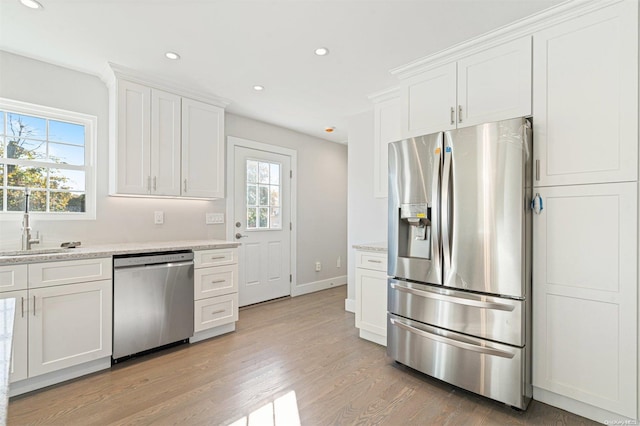 kitchen with sink, light wood-type flooring, appliances with stainless steel finishes, light stone counters, and white cabinetry