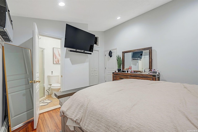 bedroom with hardwood / wood-style flooring, vaulted ceiling, a wall unit AC, and connected bathroom