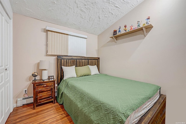 bedroom with baseboard heating, lofted ceiling, a textured ceiling, a closet, and hardwood / wood-style flooring