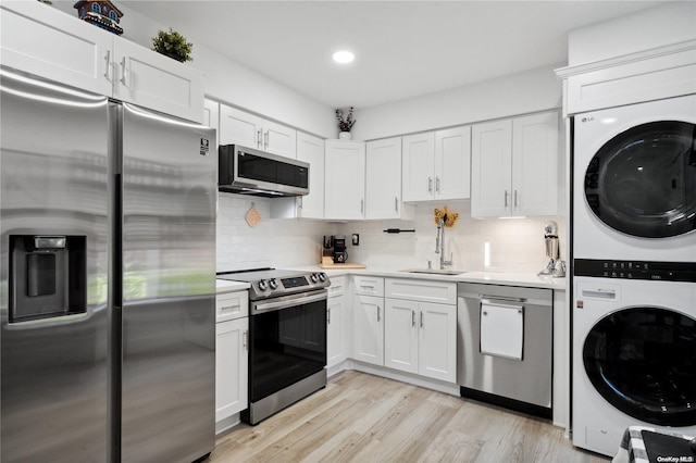 kitchen featuring sink, stacked washing maching and dryer, light hardwood / wood-style floors, white cabinets, and appliances with stainless steel finishes