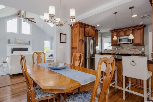 dining room featuring ceiling fan with notable chandelier, wood-type flooring, sink, and vaulted ceiling