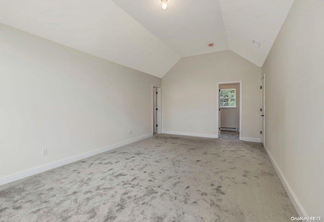 carpeted empty room with vaulted ceiling and a baseboard heating unit