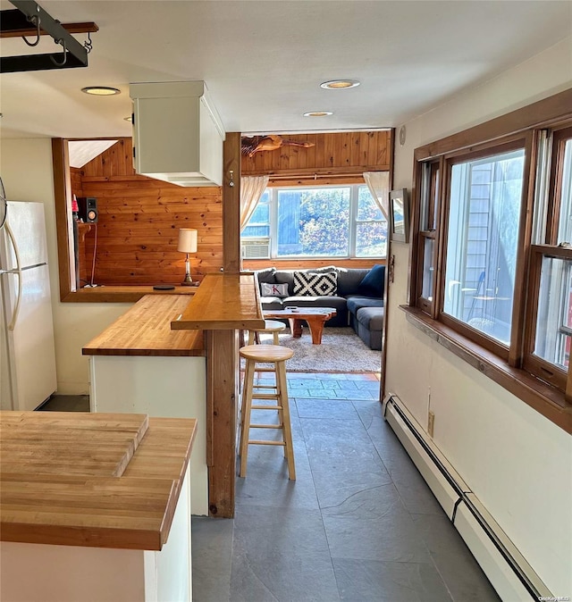 kitchen with a baseboard heating unit, butcher block countertops, wood walls, white fridge, and a breakfast bar area