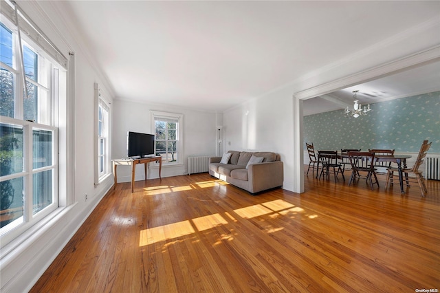 unfurnished living room featuring hardwood / wood-style floors, crown molding, radiator, and an inviting chandelier