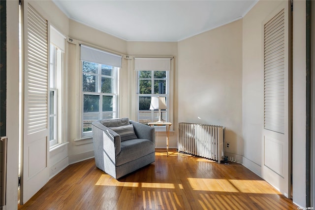 sitting room with radiator, ornamental molding, a healthy amount of sunlight, and wood-type flooring