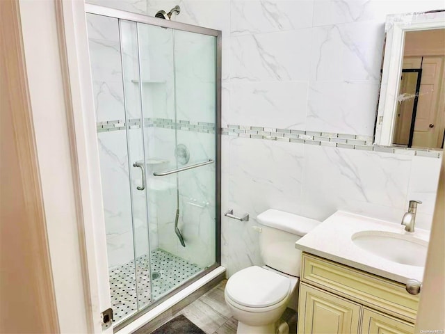 bathroom with vanity, toilet, a shower with door, and tile walls