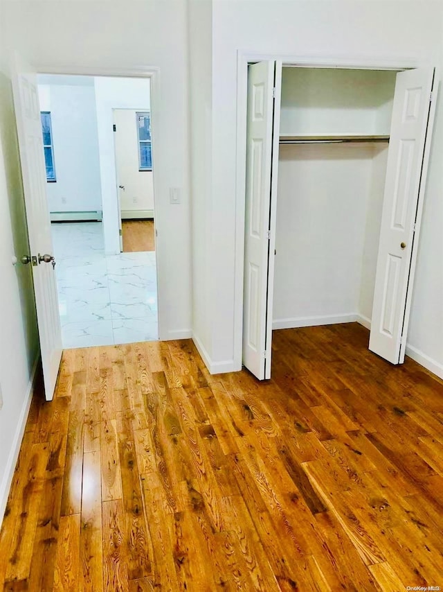 unfurnished bedroom with wood-type flooring, a closet, and baseboard heating