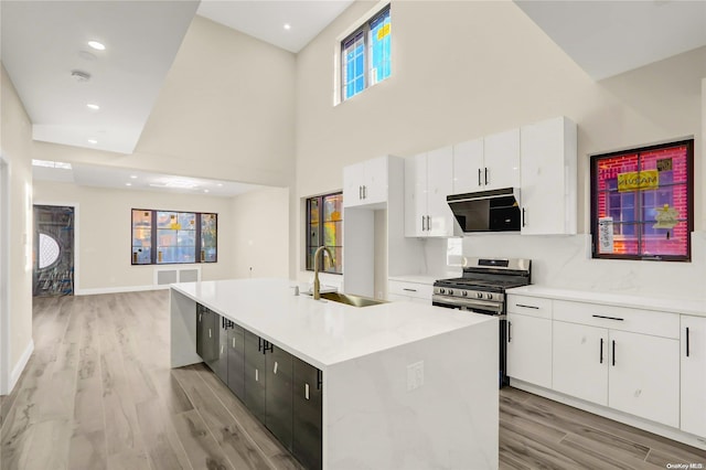 kitchen with sink, light wood-type flooring, an island with sink, gas stove, and white cabinetry