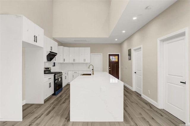 kitchen featuring a center island with sink, sink, stainless steel gas stove, light hardwood / wood-style floors, and white cabinetry