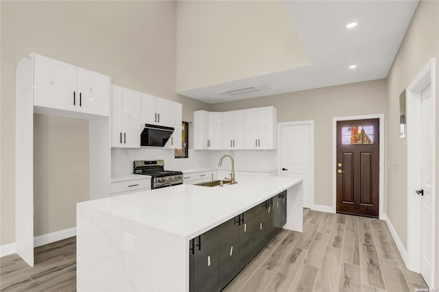 kitchen with white cabinets, gas stove, sink, and a kitchen island with sink