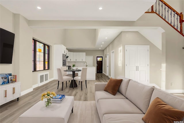 living room with light wood-type flooring, sink, and a high ceiling