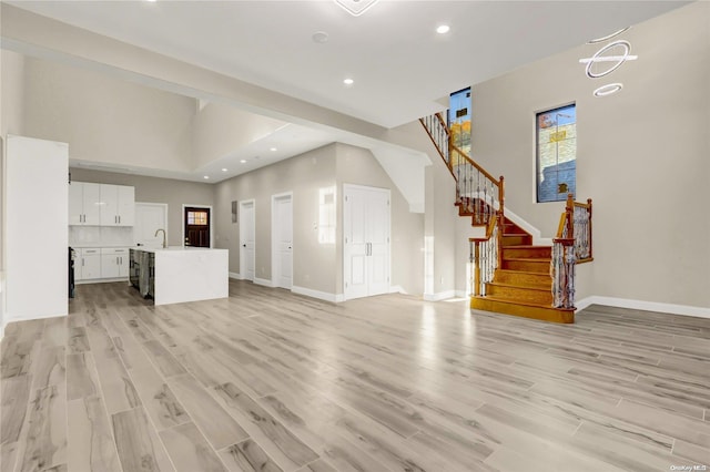 unfurnished living room featuring sink, a towering ceiling, and light hardwood / wood-style floors