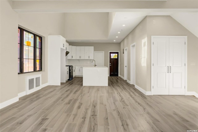 unfurnished living room with vaulted ceiling, light hardwood / wood-style flooring, and sink