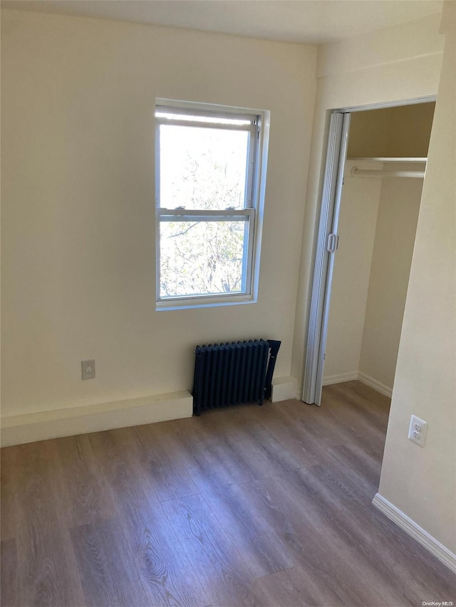 unfurnished bedroom featuring a closet, radiator heating unit, and hardwood / wood-style flooring