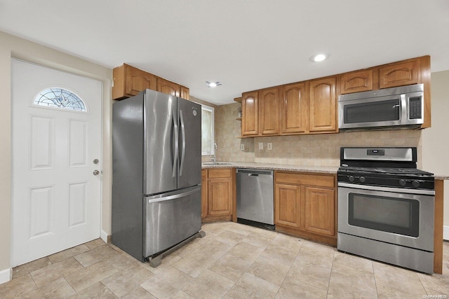 kitchen featuring decorative backsplash, light stone countertops, sink, and stainless steel appliances