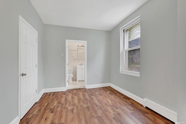 unfurnished bedroom with a baseboard radiator, ensuite bath, and hardwood / wood-style flooring