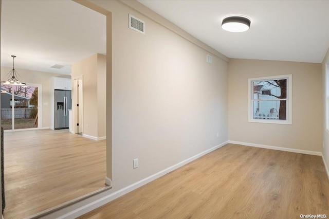 empty room with light hardwood / wood-style floors, an inviting chandelier, and lofted ceiling