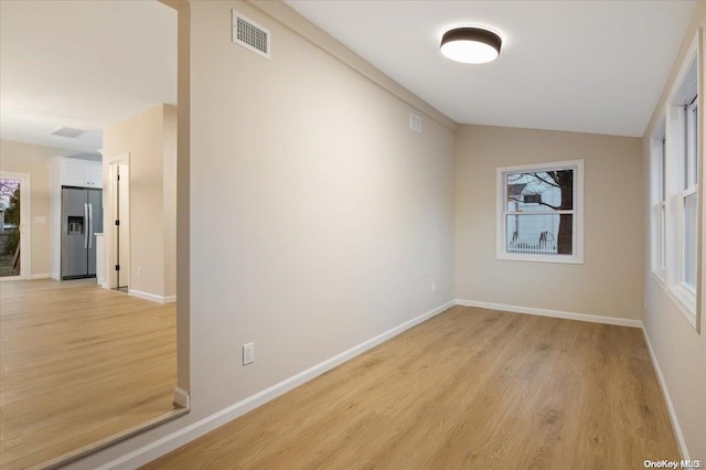 empty room featuring plenty of natural light, lofted ceiling, and light hardwood / wood-style flooring