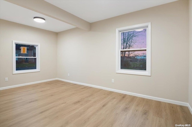 spare room featuring light hardwood / wood-style flooring and beamed ceiling