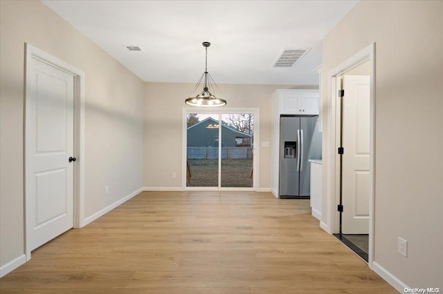 unfurnished dining area with a notable chandelier and light wood-type flooring