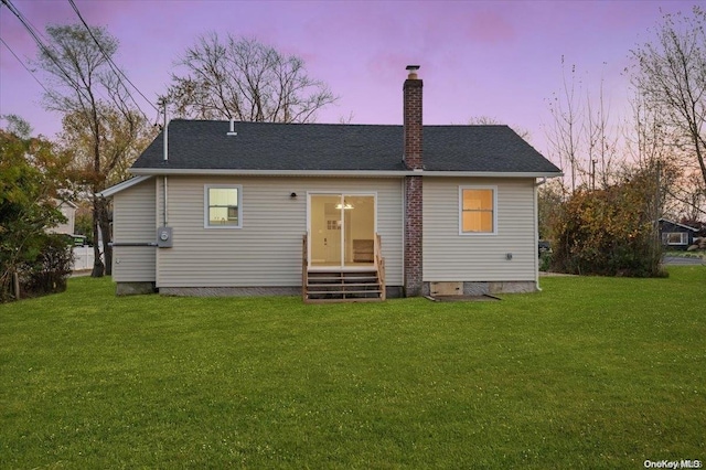 back house at dusk featuring a lawn