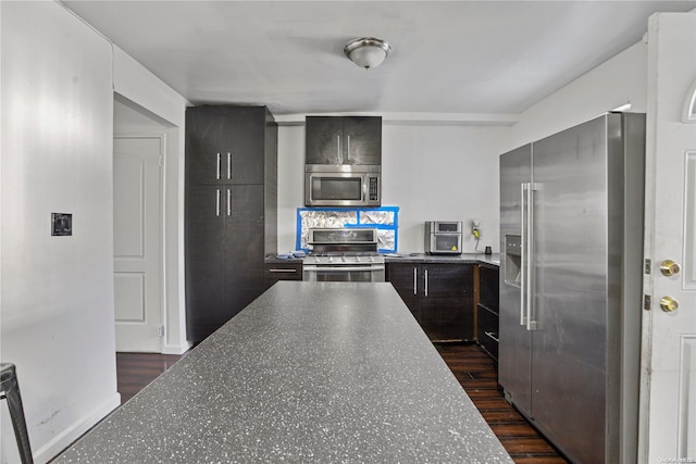 kitchen featuring dark hardwood / wood-style flooring, dark stone countertops, appliances with stainless steel finishes, and tasteful backsplash