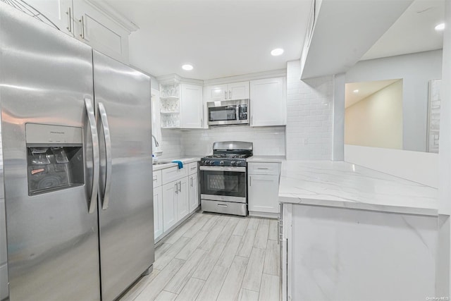 kitchen with backsplash, light hardwood / wood-style flooring, light stone counters, white cabinetry, and stainless steel appliances