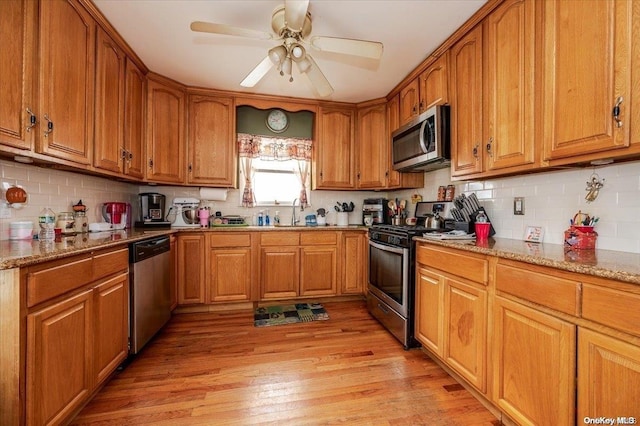 kitchen with light stone countertops, appliances with stainless steel finishes, light wood-type flooring, ceiling fan, and sink