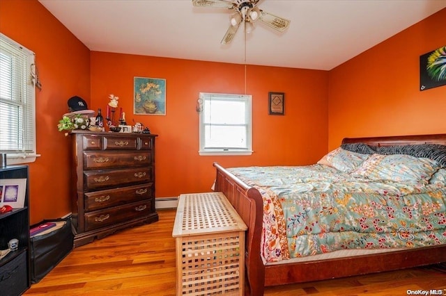 bedroom with ceiling fan, light hardwood / wood-style floors, and a baseboard heating unit