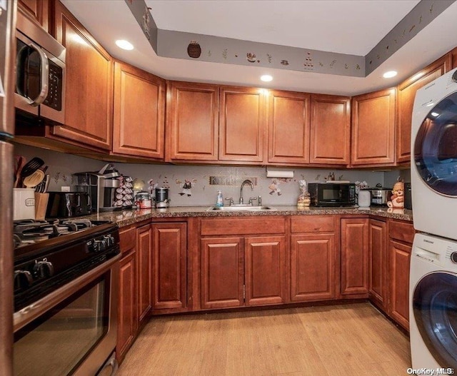 kitchen with black appliances, a raised ceiling, sink, light wood-type flooring, and stacked washer / dryer