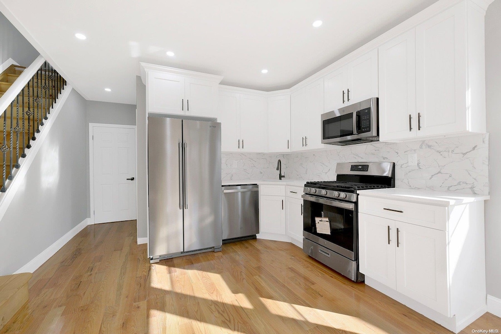 kitchen with backsplash, light hardwood / wood-style floors, white cabinetry, and stainless steel appliances