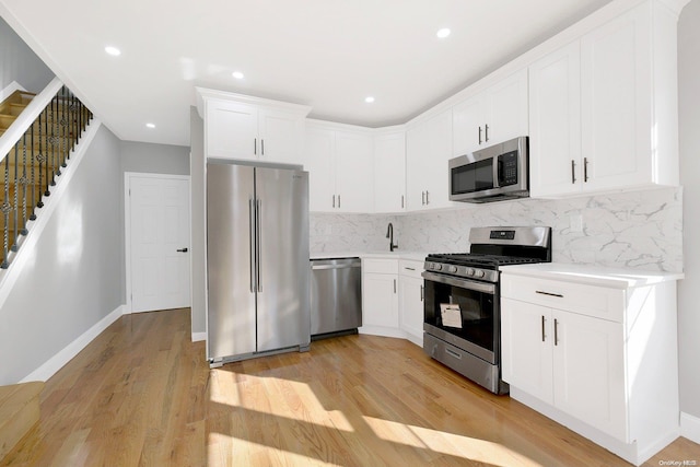 kitchen with backsplash, light hardwood / wood-style floors, white cabinetry, and stainless steel appliances