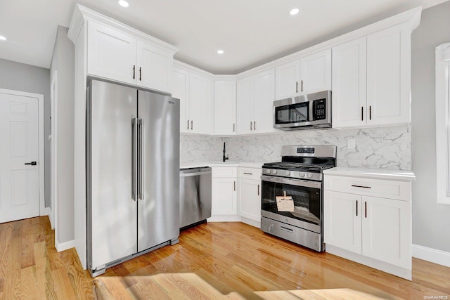 kitchen featuring white cabinets, decorative backsplash, light wood-type flooring, and appliances with stainless steel finishes