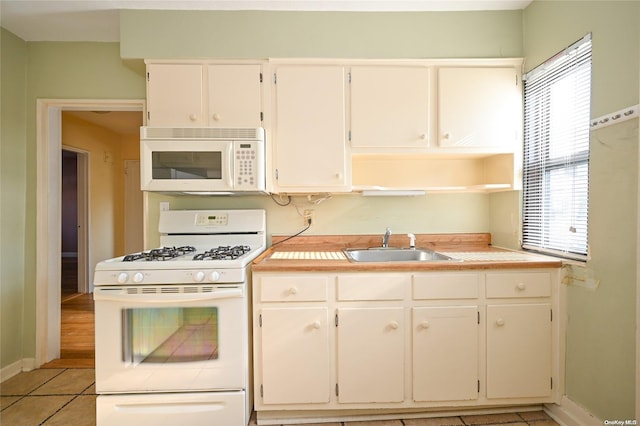 kitchen featuring light tile patterned floors, white appliances, white cabinetry, and sink