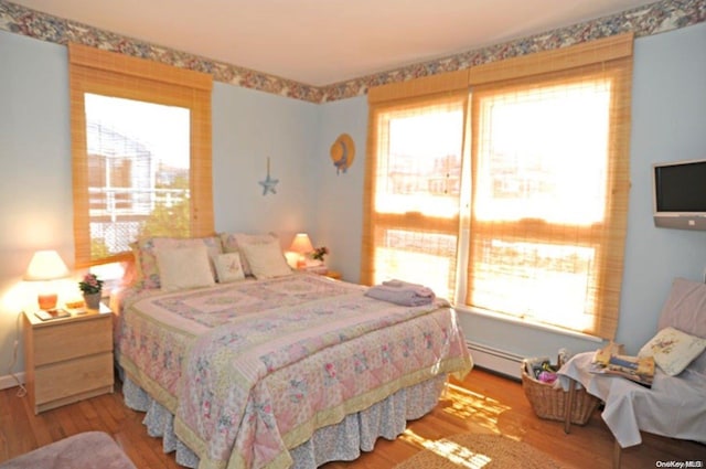 bedroom with light hardwood / wood-style floors and a baseboard heating unit