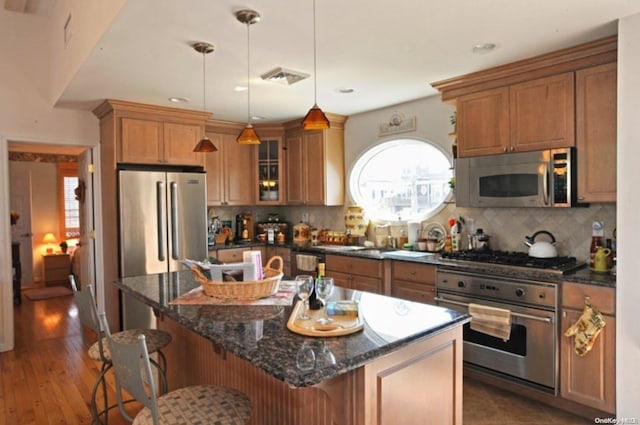 kitchen with a kitchen breakfast bar, dark hardwood / wood-style floors, decorative light fixtures, a kitchen island, and appliances with stainless steel finishes