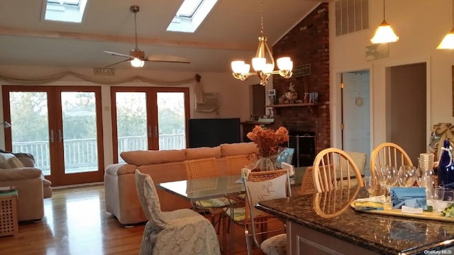 dining area with french doors, high vaulted ceiling, hardwood / wood-style floors, a fireplace, and ceiling fan with notable chandelier