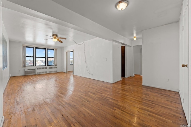 empty room with a wall mounted AC, radiator heating unit, hardwood / wood-style flooring, and ceiling fan