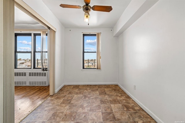 spare room with a wealth of natural light, ceiling fan, radiator, and hardwood / wood-style floors