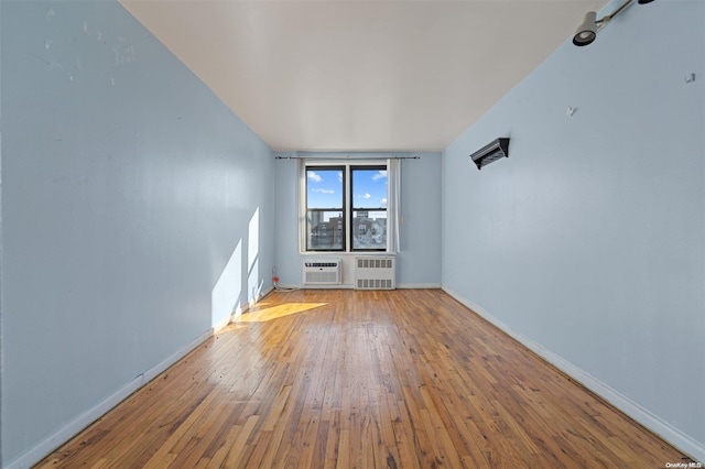 spare room featuring hardwood / wood-style floors, a wall mounted air conditioner, and radiator heating unit