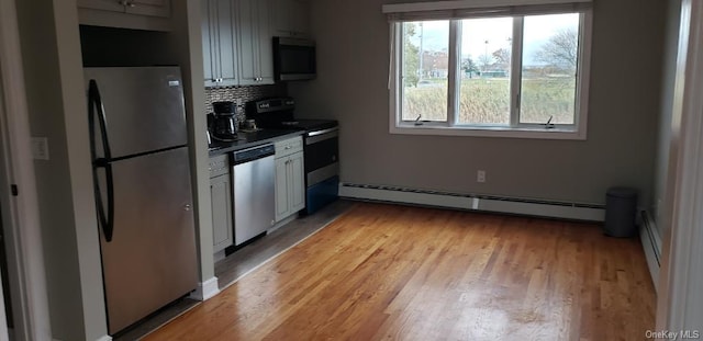 kitchen with backsplash, white cabinets, appliances with stainless steel finishes, a baseboard radiator, and light hardwood / wood-style floors