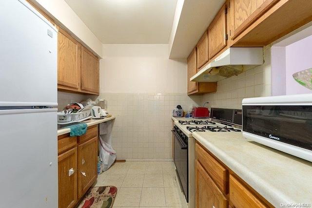 kitchen featuring white fridge, gas range oven, tile walls, and light tile patterned floors