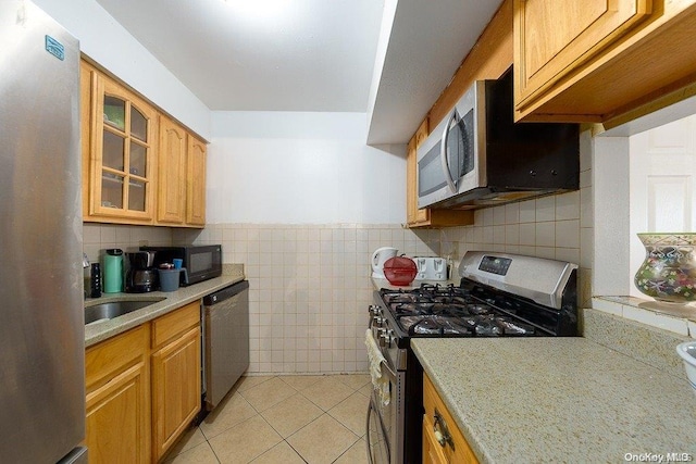 kitchen with light stone countertops, stainless steel appliances, sink, tile walls, and light tile patterned flooring