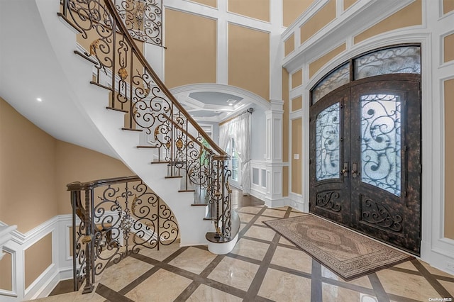 foyer entrance featuring decorative columns, a towering ceiling, ornamental molding, and french doors