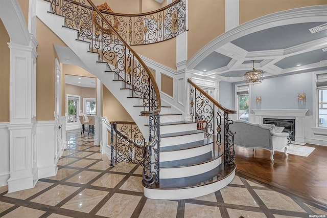 stairs featuring decorative columns, crown molding, plenty of natural light, and coffered ceiling